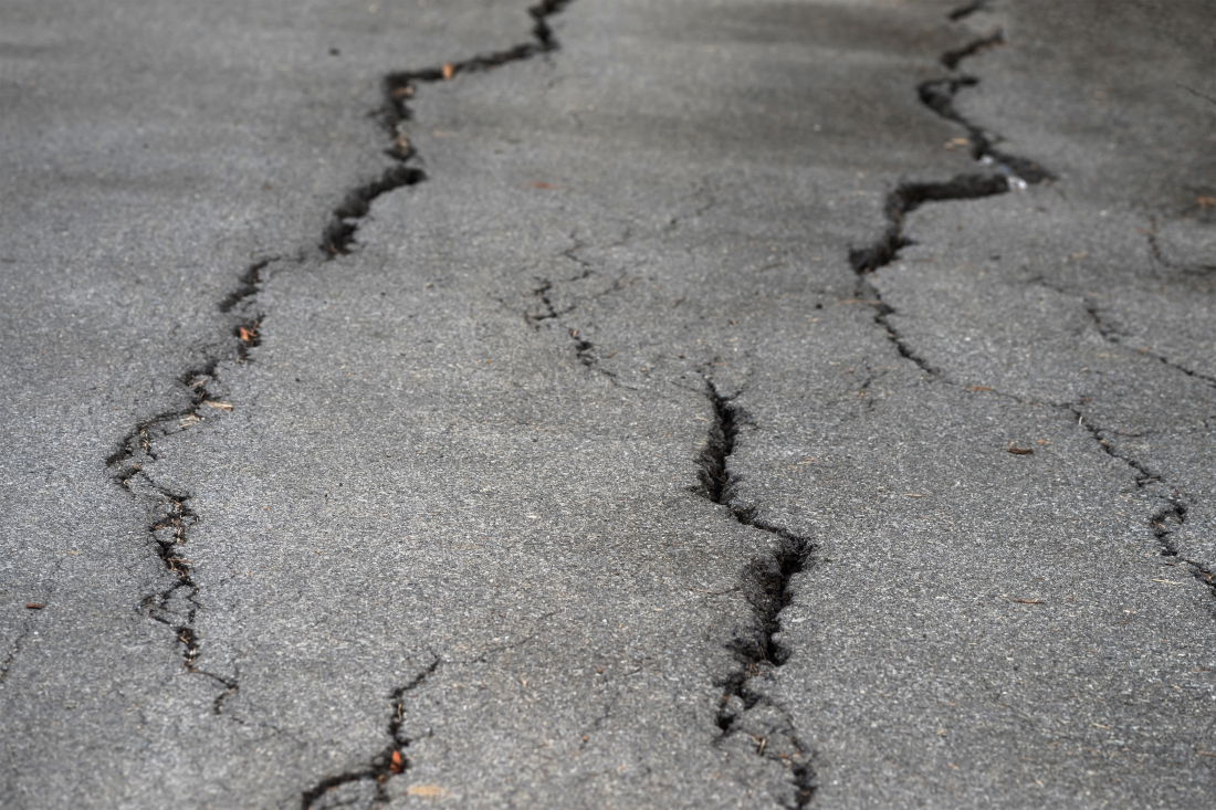 Closeup photo of cracked asphalt in local road or street after earthquake or el nino. Textured pattern background. Natural disaster.